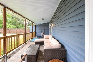 Une véranda couverte avec une balustrade en bois, un coin salon avec des coussins et un fauteuil suspendu.