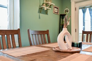 Une table à manger avec deux chaises en bois, un vase blanc à la forme originale et une petite pile de livres.
