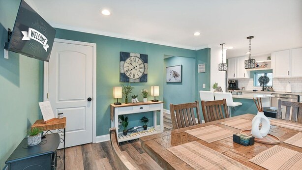 Une cuisine moderne avec des meubles blancs, une table à manger en bois avec des sets de table et une horloge au mur.