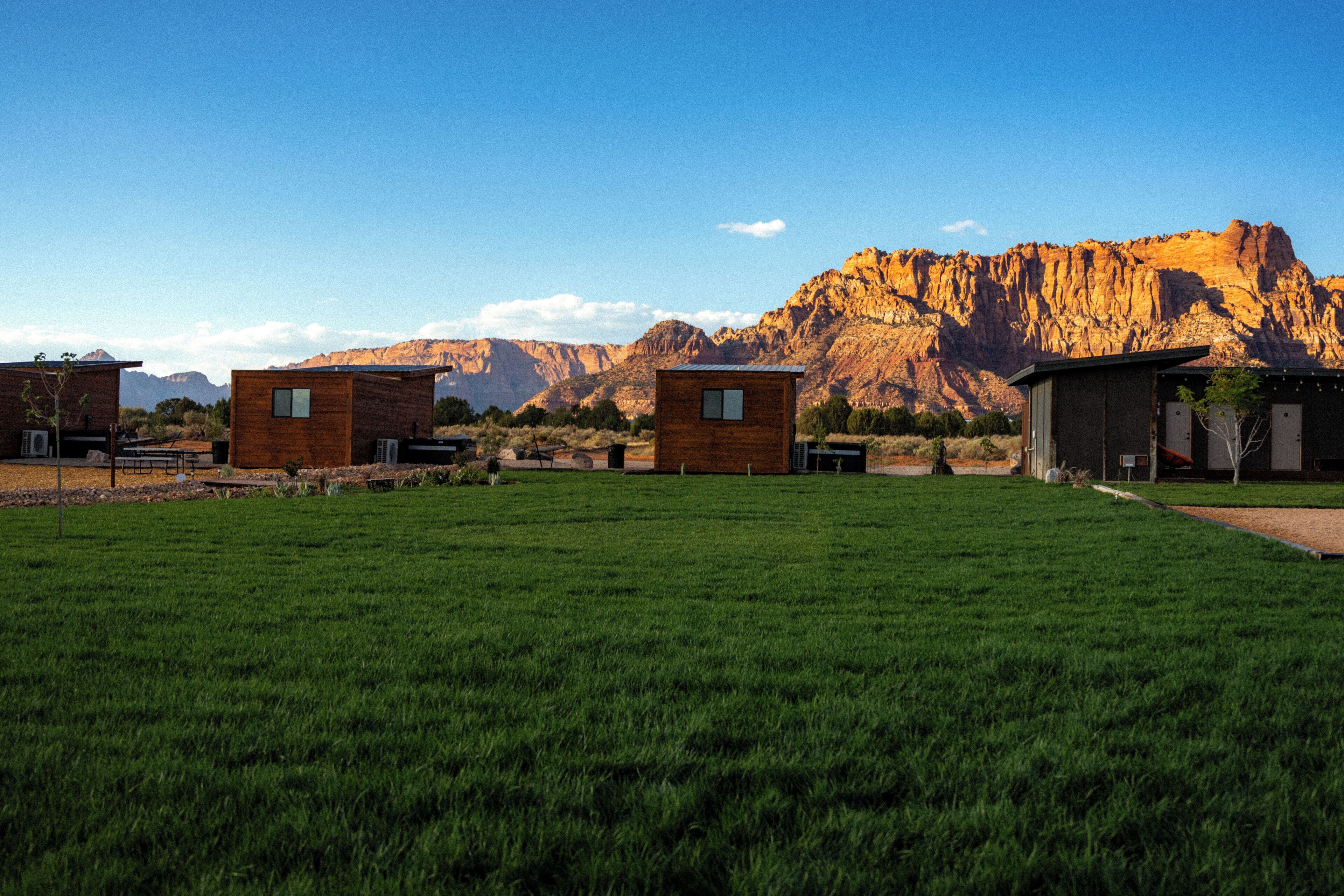 A grassy field with several wooden cabins and a mountain in the background.