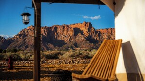 Paisaje desértico con una montaña al fondo, una silla de madera y un farol bajo una tienda de campaña.