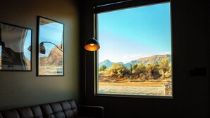 Una habitación con un ventanal grande, un sofá de cuero marrón, una mesa con un libro y dos cuadros en la pared.