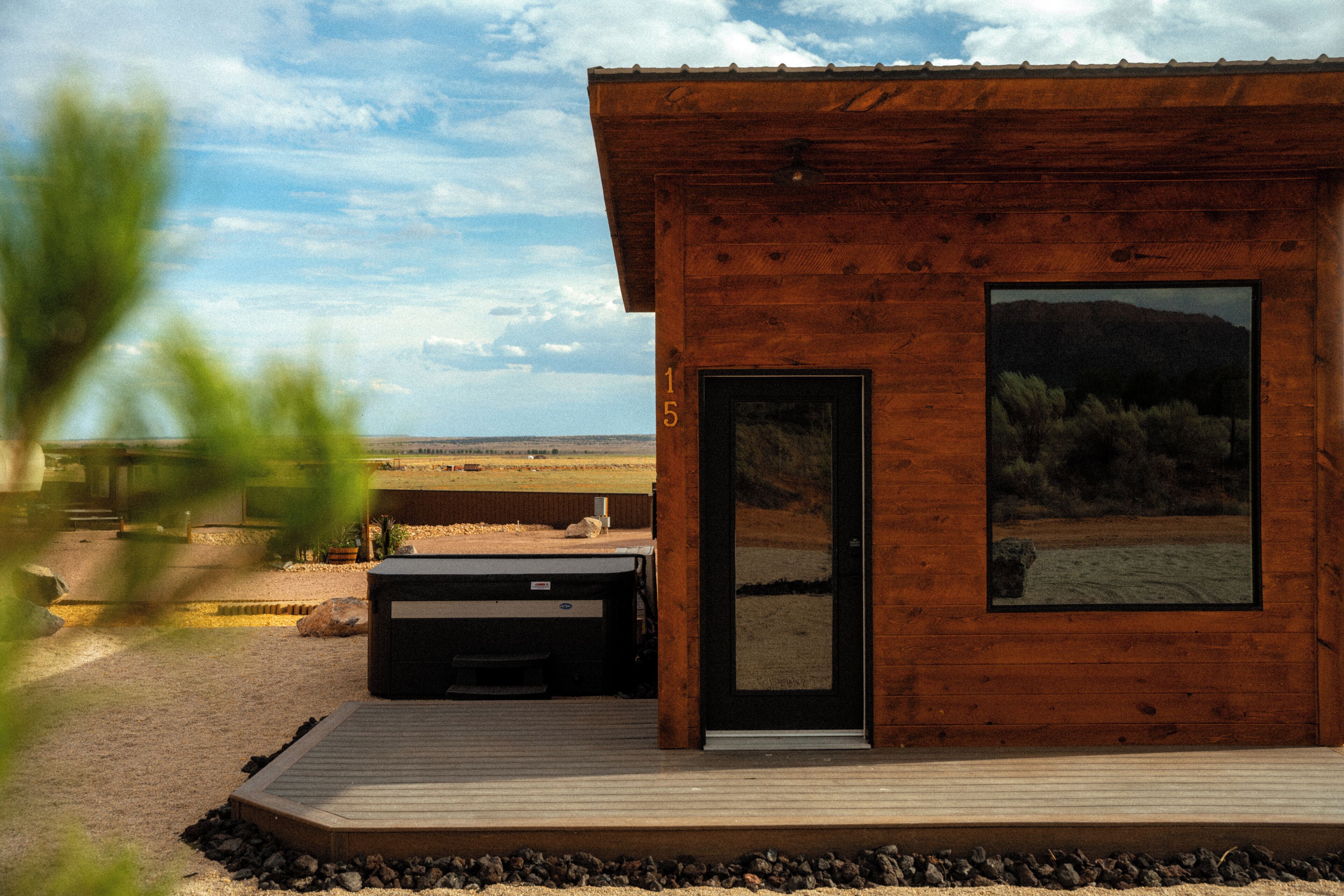 A wooden cabin with a large window, a door, and a hot tub outside.