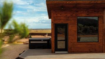 A wooden cabin with a large window, a door, and a hot tub outside.