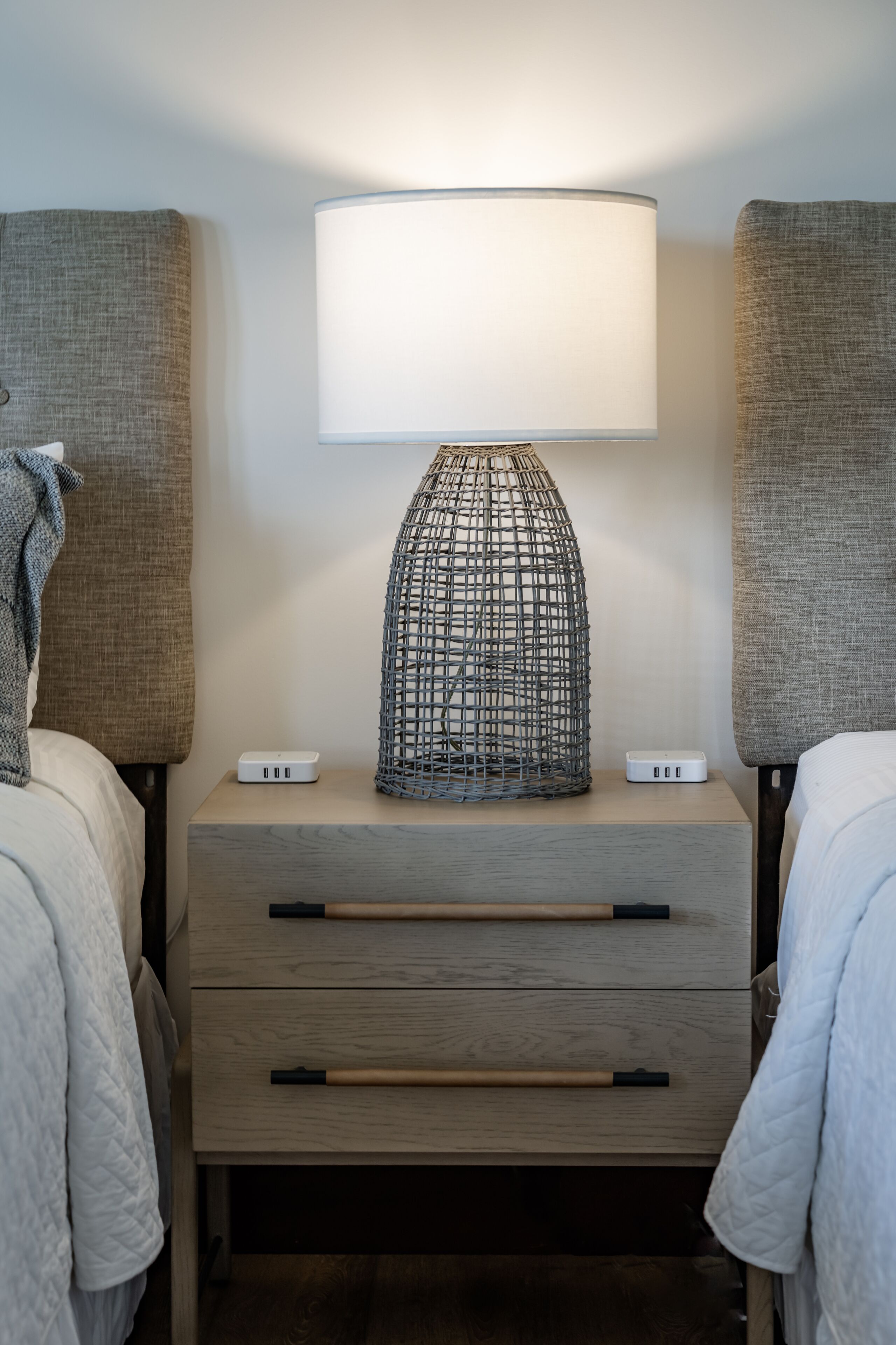 Ein ordentlich eingerichtetes Schlafzimmer mit Nachttischlampe, zwei Nachttischen und einer Schubladeneinheit.
