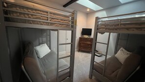 Une chambre avec des lits superposés, une commode en bois et un téléviseur à écran plat.