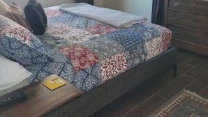 Un dormitorio con una cama, un televisor montado en la pared, una ventana con cortinas y un aparador de madera.