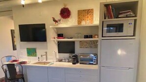 Cocina compacta con armarios blancos, microondas, tostadora y pileta.