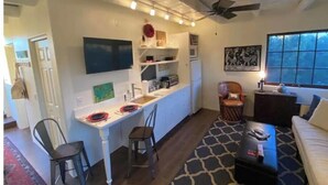 Un espacio habitable compacto con kitchenette, comedor y zona de estar con sofá y sillones.