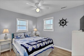 A bedroom with a bed, two bedside tables, a ceiling fan, and a ship's wheel decoration. - "Island Time", Peaceful 5BR Oceanfront Cottage (Surf City)