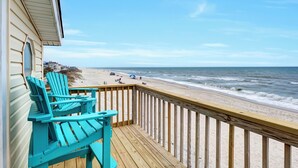 A wooden deck with turquoise Adirondack chairs overlooking a beach with people and a boardwalk. - "Island Time", Peaceful 5BR Oceanfront Cottage (Surf City)