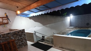 A rooftop pool area with a stone wall, a small bar area with stools, and a staircase leading to the pool.