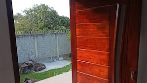 A wooden door with a keyhole, leading to an outdoor area with a concrete floor, a brick wall, and a grassy patch.