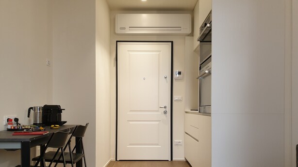 A compact kitchen with a white door, a coffee machine, and a small dining area with chairs. - Exclusive suite in the historic center (Bologna)