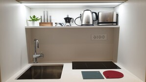 A compact kitchen with a sink, a stovetop, and a countertop with a kettle, a coffee maker, and a plant. - Exclusive suite in the historic center (Bologna)