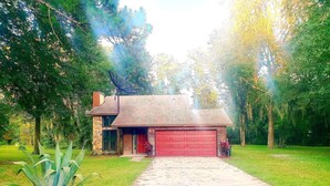 Una casa de dos pisos con una puerta de garaje roja, rodeada de exuberante follaje y árboles.