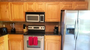 Una cocina con armarios de madera, un refrigerador de acero inoxidable, un microondas, una estufa y una cafetera.
