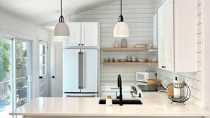 A modern kitchen with a large island, black bar stools, pendant lights, and white cabinetry. - Sparkling East Hampton Oasis 3 bed 2 bath w/heated pool. Pets Welcome! (East Hampton)
