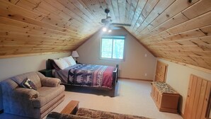 Ein gemütliches Schlafzimmer im Dachgeschoss mit schrägen Wänden, einem Bett mit gemusterten Betttextilien, einer Couch und einer kleinen Holzbank.