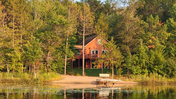 Eine Holzhütte mit einer Terrasse, umgeben von dichtem Wald und einem See.