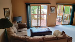 Ein Wohnzimmer mit einer Couch, einem Fernseher und einer Schiebetür zu einer Terrasse.