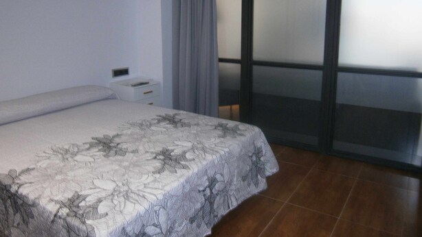A bedroom with a bed, a nightstand, and a large window with a view.