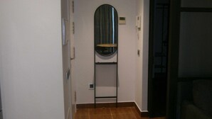 A narrow hallway with a tiled floor, a door with a mirror, and a small shelf.