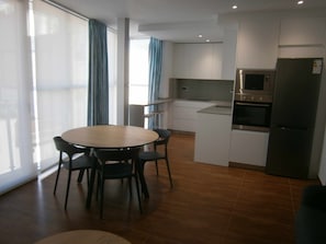 A modern kitchen with white cabinets, a stainless steel refrigerator, and a built-in oven. There is a dining area with a round table and chairs. - "Xot" 1bedroom+Sofa-bed 2/4 peoples, Streetview, centre village (Sant Carles De La Rapita)