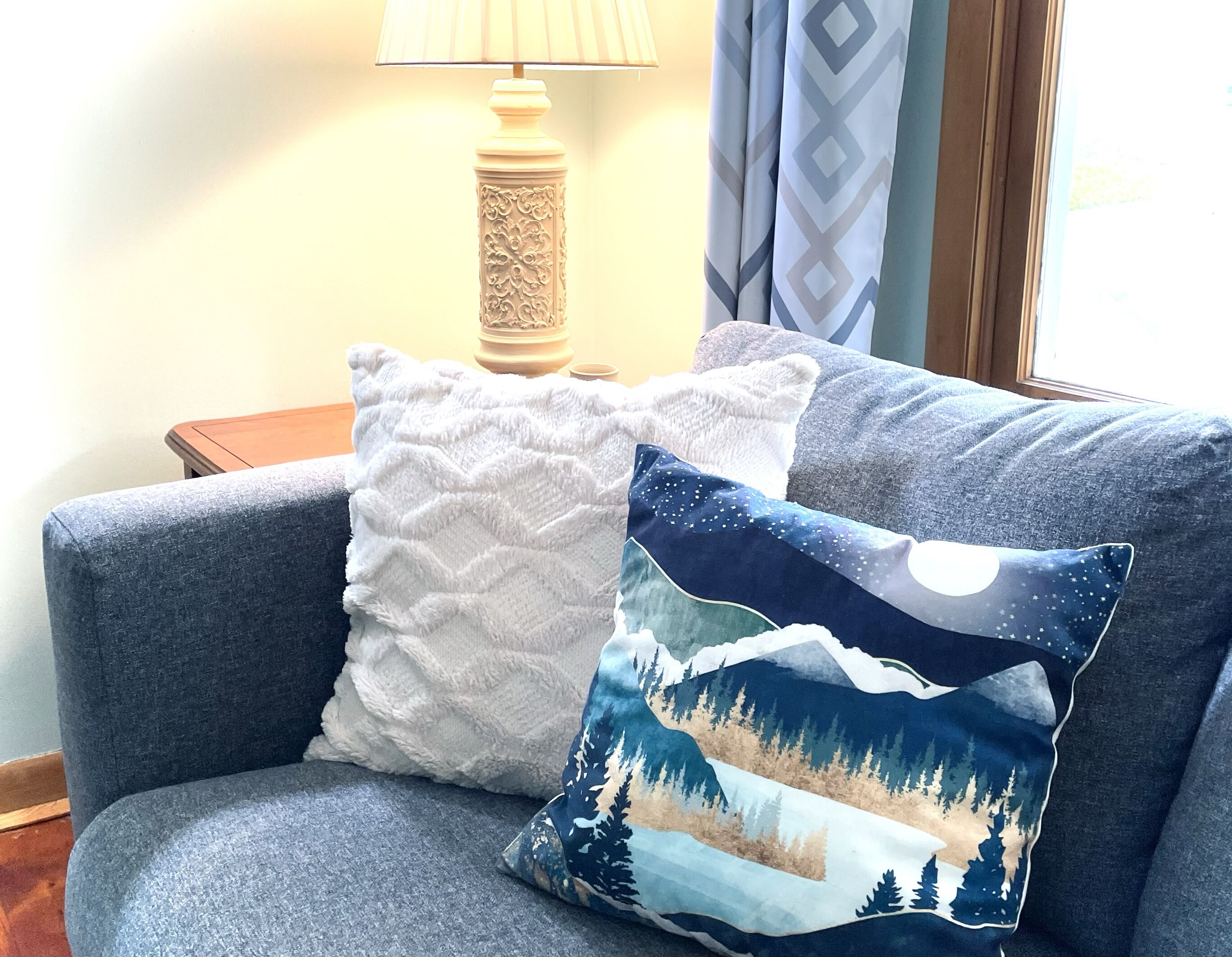 Ein blaues Sofa mit zwei Zierkissen, einer Lampe und einem Fenster mit Vorhängen.