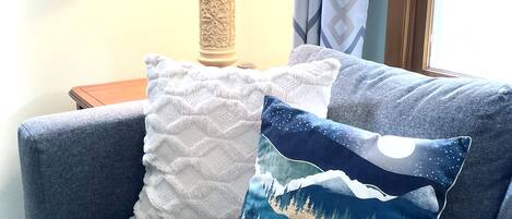 Ein blaues Sofa mit zwei Zierkissen, einer Lampe und einem Fenster mit Vorhängen.