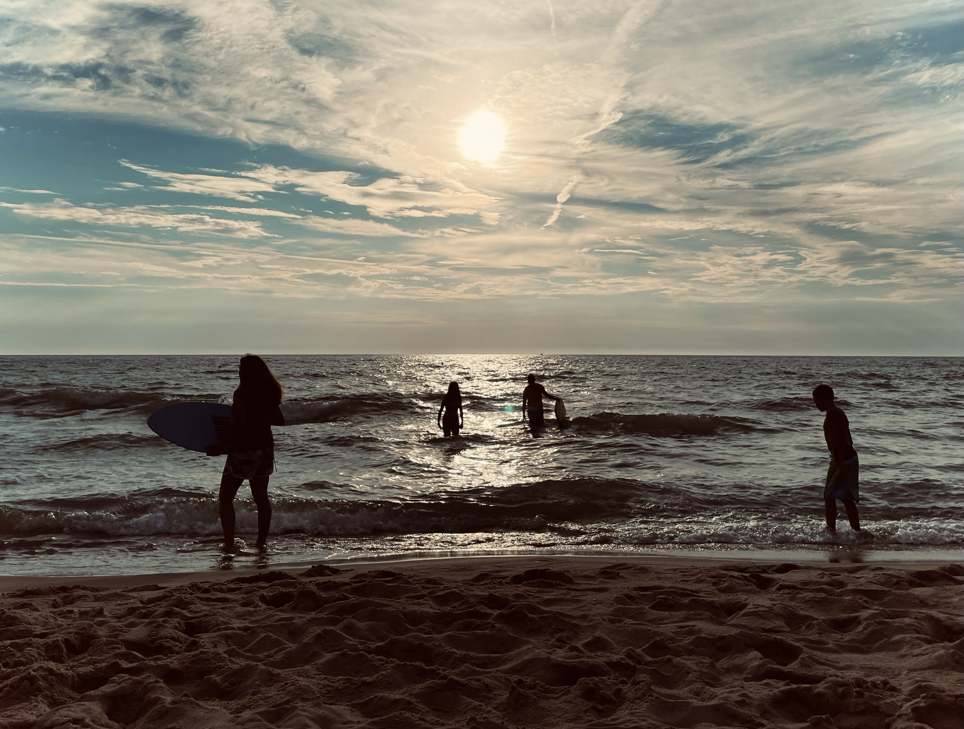A beach scene with people standing in the water and on the sand, holding surfboards.