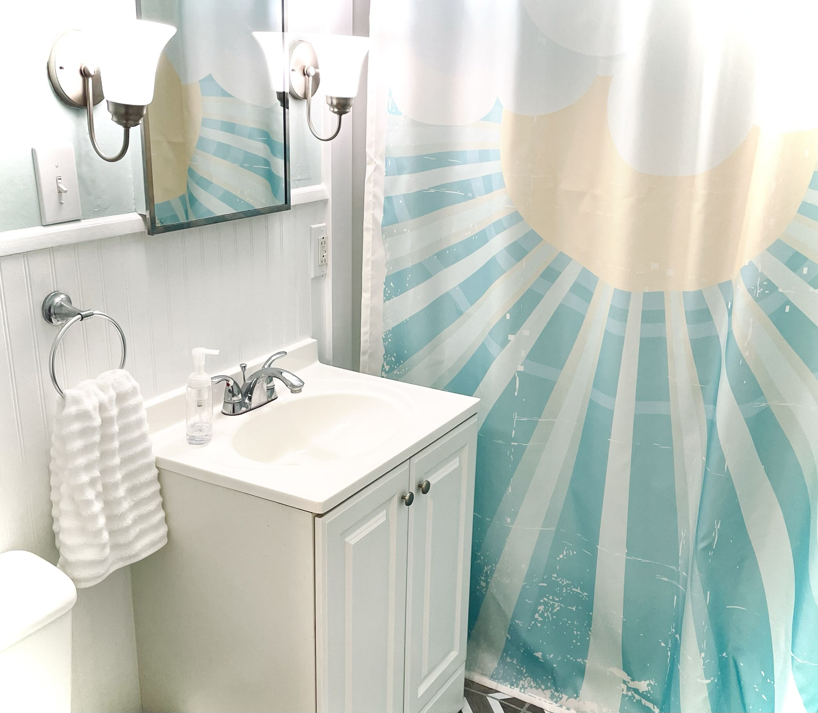 A bathroom with a sink, mirror, towel ring, and a shower curtain with a sunburst pattern.