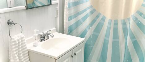 A bathroom with a sink, mirror, towel ring, and a shower curtain with a sunburst pattern.