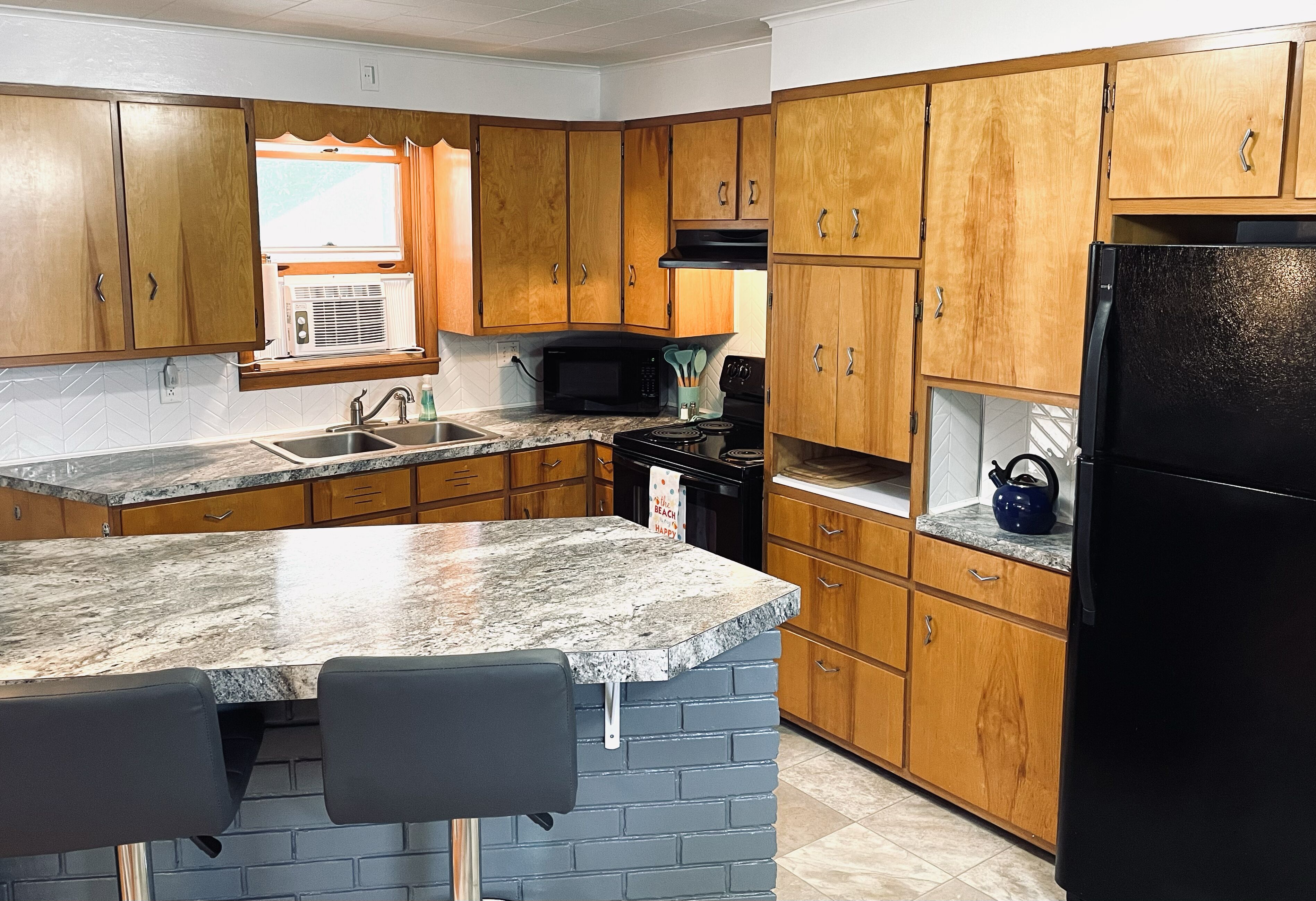 A kitchen with wooden cabinets, a granite countertop, a black refrigerator, and a microwave.