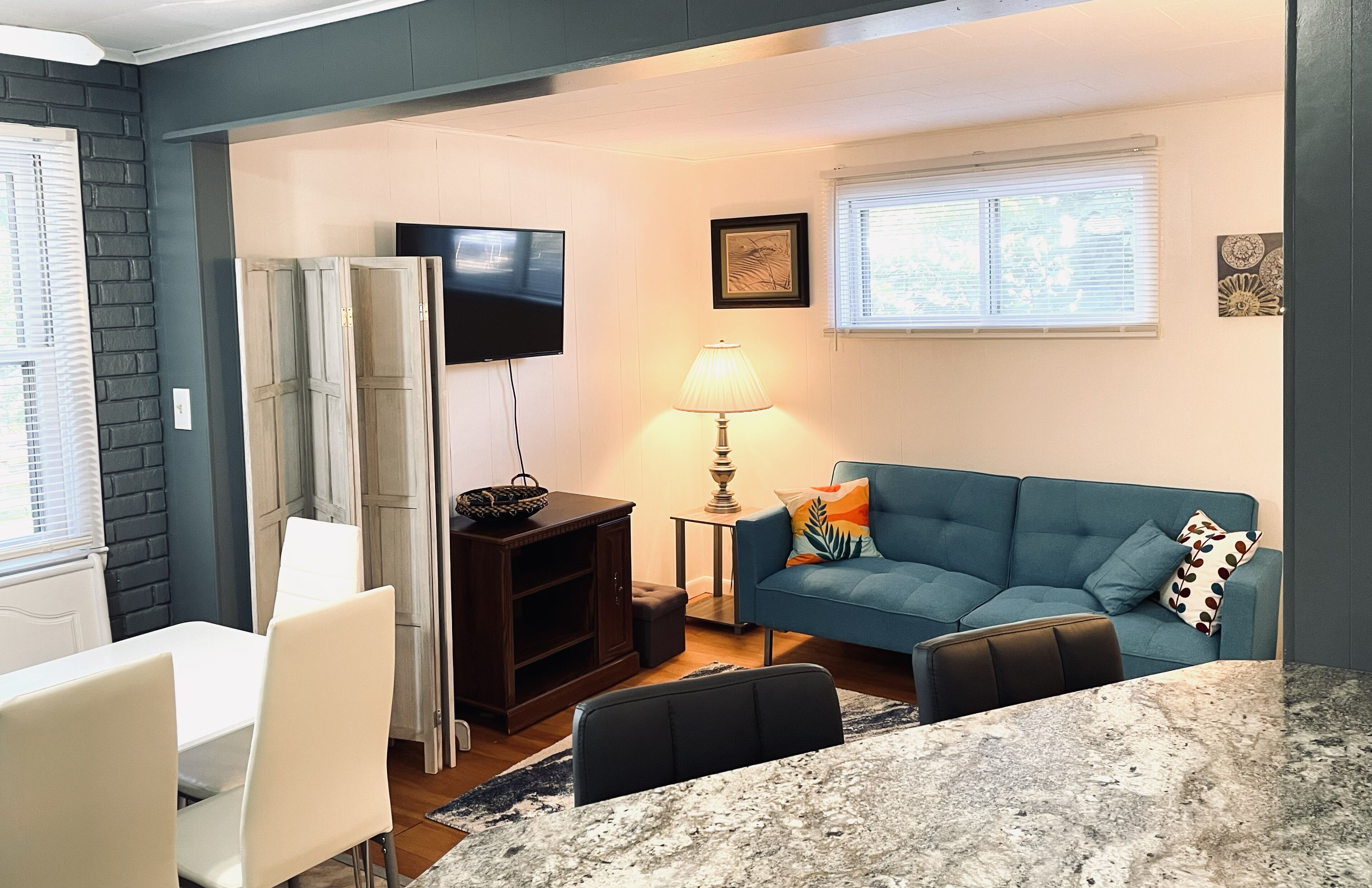Una sala de estar moderna con un sofá azul, un televisor, una lámpara y una zona de comedor con una mesa y sillas.