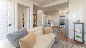 A modern living room with a beige sofa, a coffee table, and a bookshelf. - Enjoy this Brand New Cozy 2BR Guest Suite in YYC! (Calgary)