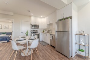 Une cuisine moderne avec des meubles blancs, un réfrigérateur en acier inoxydable et un coin repas comprenant des chaises blanches et une table ronde.