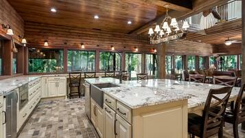 A spacious kitchen with a large island, wooden ceiling, and large windows offering a view of the outdoors.