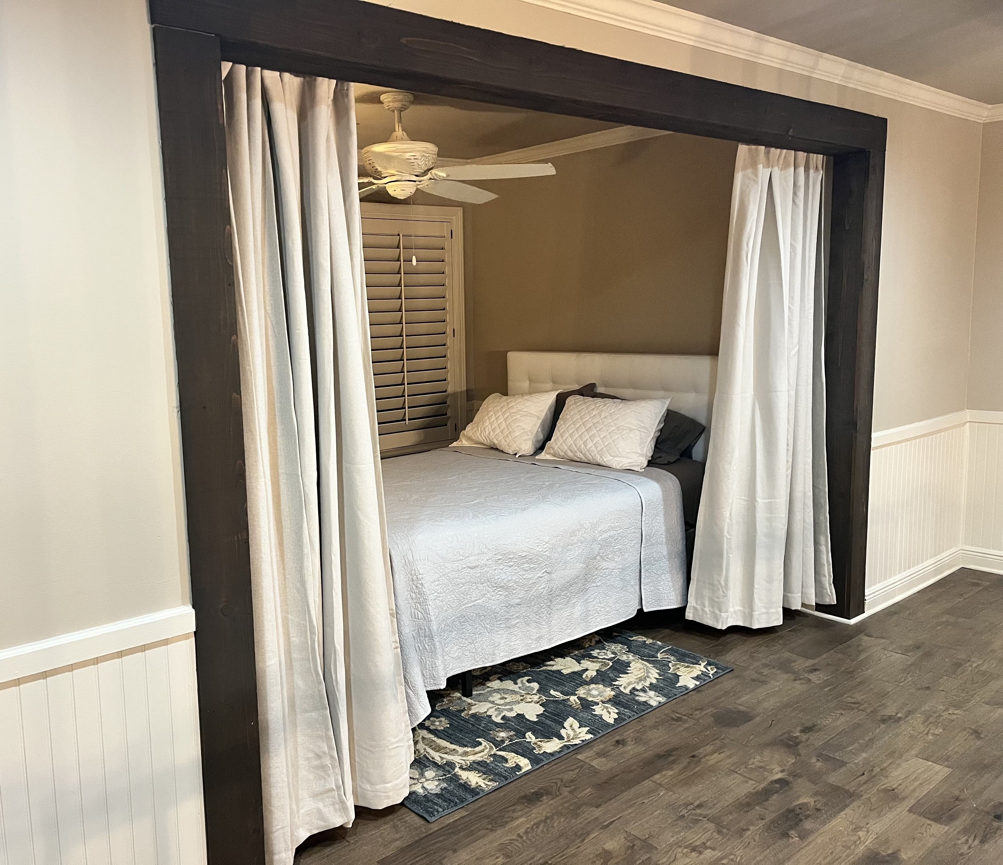 A bedroom with a bed, curtains, a ceiling fan, and a patterned rug.