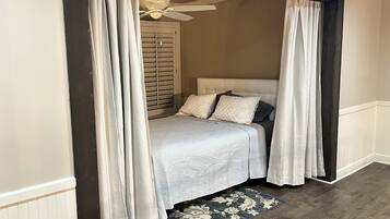 A bedroom with a bed, curtains, a ceiling fan, and a patterned rug.