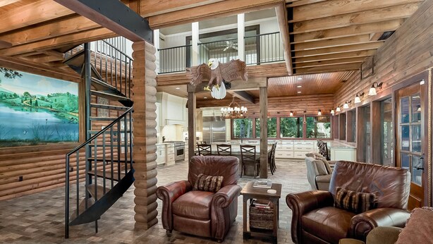 A spacious interior with a wooden staircase, leather armchairs, a dining area, and large windows offering views of the outdoors. - Spacious Riverside Lodge on 370 acres near Tuscaloosa, 8 bedrooms - sleeps 15 (Gordo)