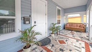 Eine Veranda mit Fliesenboden, einer weißen Tür und einem braunen Sofa.