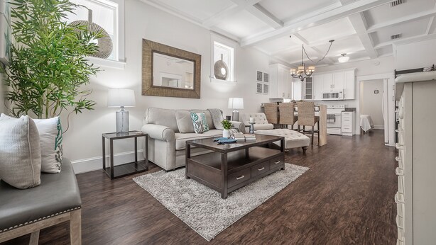 Ein modernes Wohnzimmer mit einem dunklen Holztisch, einem beigen Sofa und einer großen, grünen Pflanze.