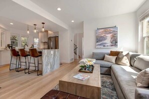 A modern kitchen with bar stools, a marble island, and pendant lighting.