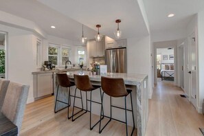 A modern kitchen with a central island, bar stools, stainless steel appliances, and pendant lighting.