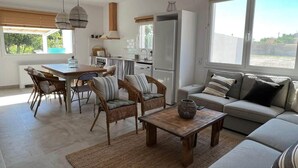 A modern kitchen with white cabinets, a refrigerator, and a dining area with wicker chairs and a wooden table. - Mas Midó. Masia Restaurada en Delta del Ebro (Sant Jaume d'Enveja)