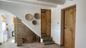 A modern interior with a staircase leading to a kitchen area, featuring exposed brick walls, wooden doors, and woven baskets on the wall. - Mas Midó. Masia Restaurada en Delta del Ebro (Sant Jaume d'Enveja)