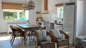 A modern kitchen with a dining area, wicker furniture, and a large refrigerator. - Mas Midó. Masia Restaurada en Delta del Ebro (Sant Jaume d'Enveja)