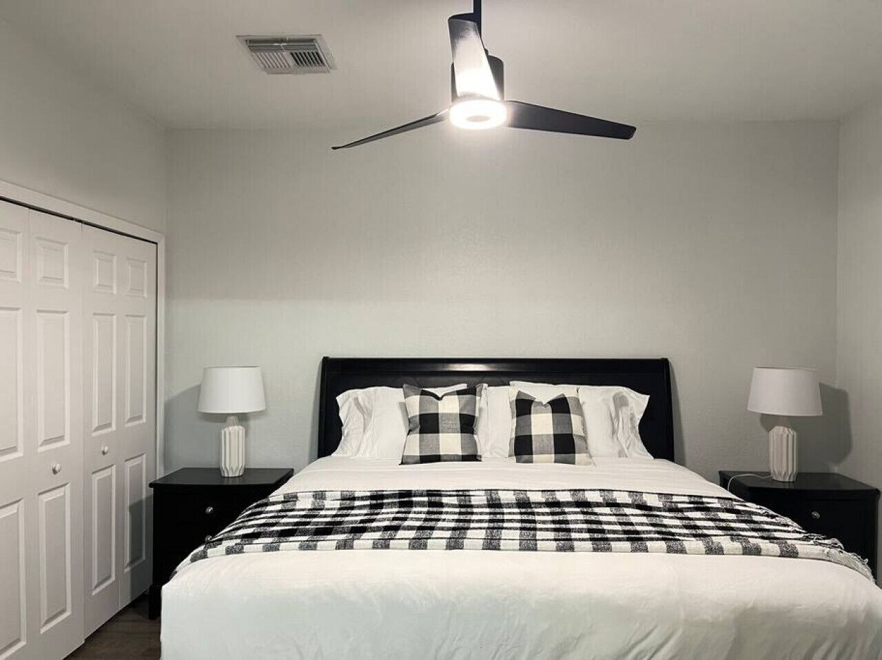 A bedroom with a bed, two bedside tables with lamps, a ceiling fan, and a white wardrobe.