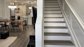 En trappa med modern design, ett matområde med ett träbord och stolar samt ett köksområde med en kristallkrona.